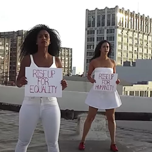 Tres mujeres de blanco de pie en una azotea con carteles de justicia social