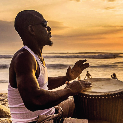 Musician playing drums on beach with sunset background