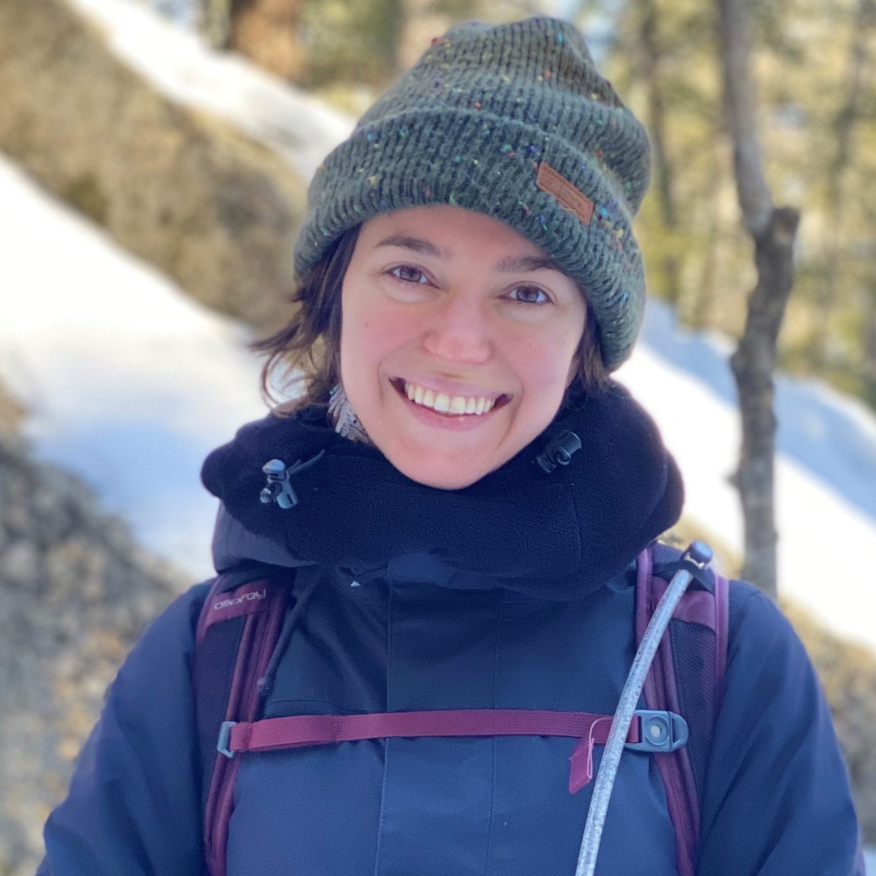 Square cropped headshot of team member Sam Zimmer outdoors in winter hiking gear.
