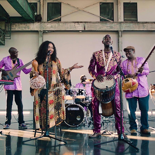 A group of seven Black musicians wearing traditional West African clothing performing a concert in the WaterFire Arts Center