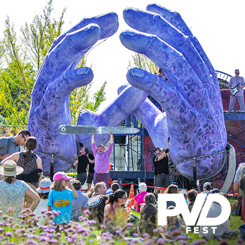 A pair of giant purple hands frame a stage with musicians performing