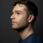 Profile of Shane Larson a white man with light brown hair wearing a navy blue t-shirt
