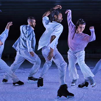 A group of ice skaters dressed in white and light purple, captured in active moves on the ice