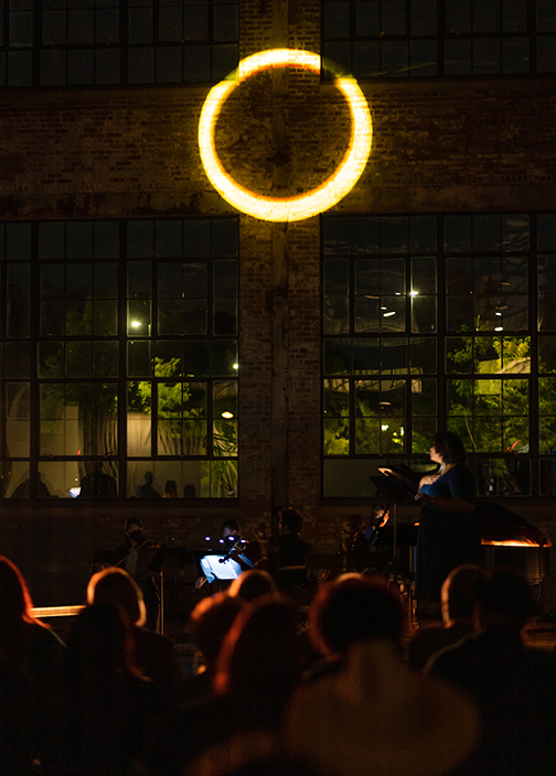 In a darkened performance space an audience watches a white ring of light projected on a wall
