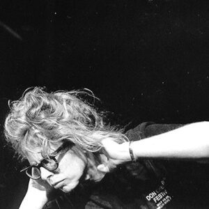 A black and white portrait of a middle aged white woman holding her hands up by her ears