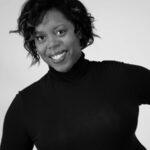 A black and white headshot of a smiling adult Black woman with a short wavy bob haircut wearing a black turtleneck shirt