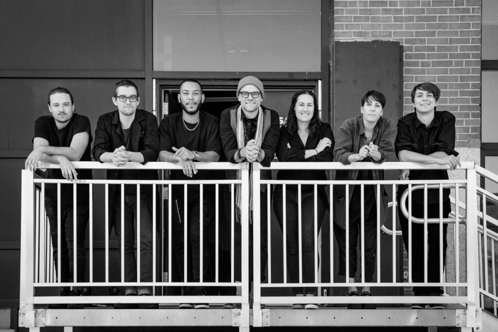 A black and white group portrait of seven adults standing behind a white railing