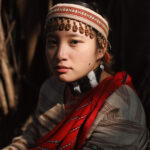 A young Indigenous Asian woman wearing a red and white headband and a red scarf over a grey tunic top
