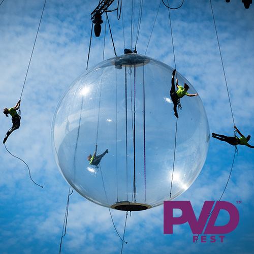 A transparent sphere set against a blue sky lightly dusted with cirrus clouds. Aerial dancers perform inside and around the sphere