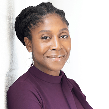 A Black woman wearing a plum Nehru collar blouse and with her hair pulled back shown in three-quarter view from the shoulders up against a white background