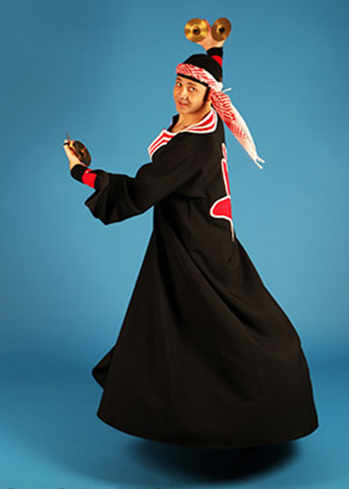 A man in flowing black robes with red details spins with his right arm held high over his head and his left arm held out in front