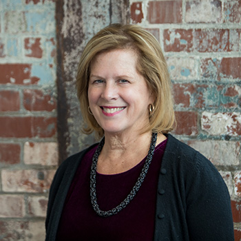 Headshot of Kathleen Pletcher a woman with chin length blond hair wearing a black top and necklace